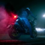 Un piloto y una moto naked de 125 cc vista desde atrás y abajo en plena noche y con las luces encendidas