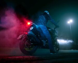 Un piloto y una moto naked de 125 cc vista desde atrás y abajo en plena noche y con las luces encendidas