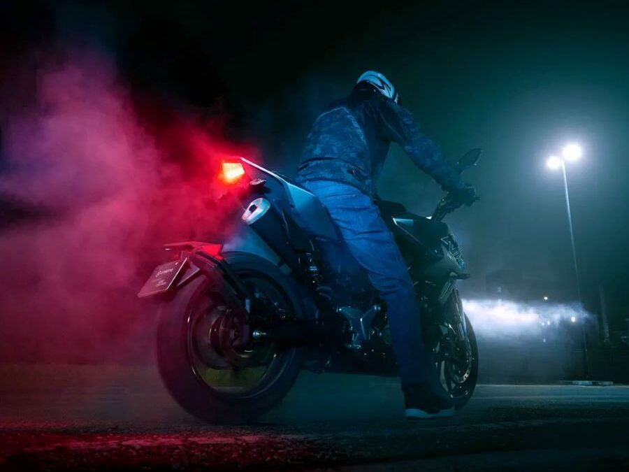 Un piloto y una moto naked de 125 cc vista desde atrás y abajo en plena noche y con las luces encendidas