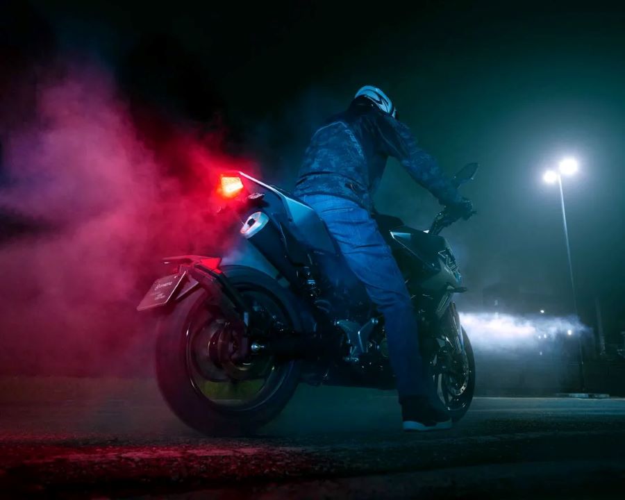 Un piloto y una moto naked de 125 cc vista desde atrás y abajo en plena noche y con las luces encendidas