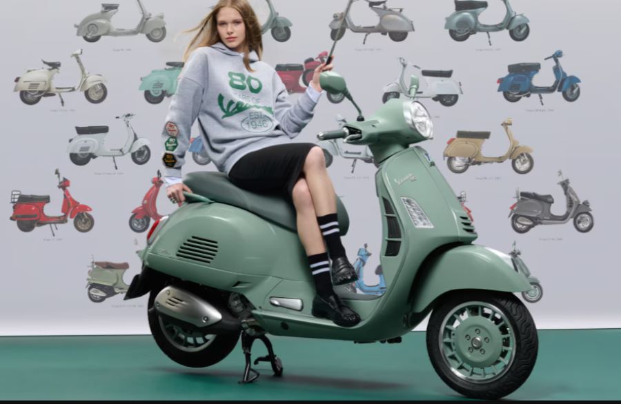 una adolescente posa sobre una moto Vespa Primavera 80th verde pastel