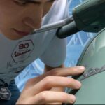 Un joven se acerca una moto Vespa 80Th para tocar el logotipo corpóreo metálico