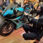 Una modelo china en cuclillas señala a su derecha a la moto Guruma 1000 RR durante una exposición