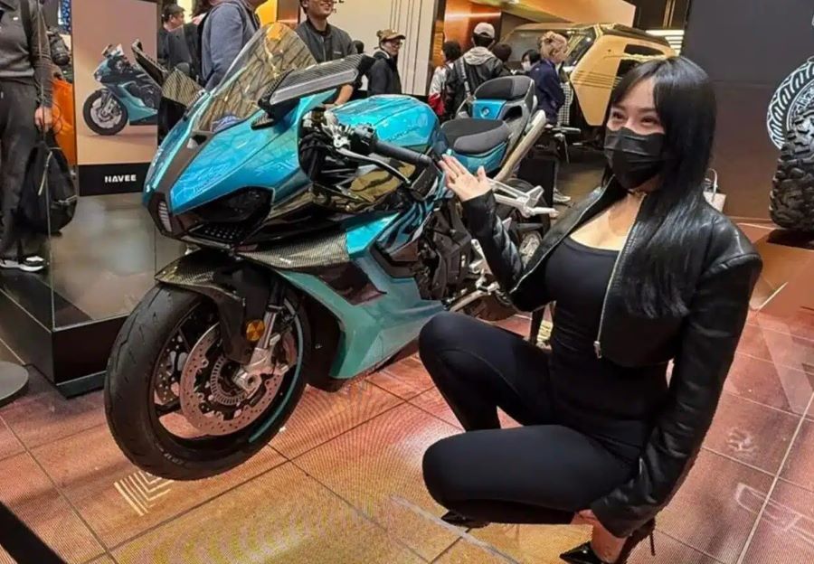 Una modelo china en cuclillas señala a su derecha a la moto Guruma 1000 RR durante una exposición