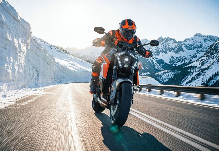 Una KTM 1390 Super Duke RR 2026 viene de frente en una carretera bordeada por montañas nevadas
