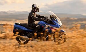 Una moto K1600 GT azul pasa delante de una maleza otoñal en una ruta