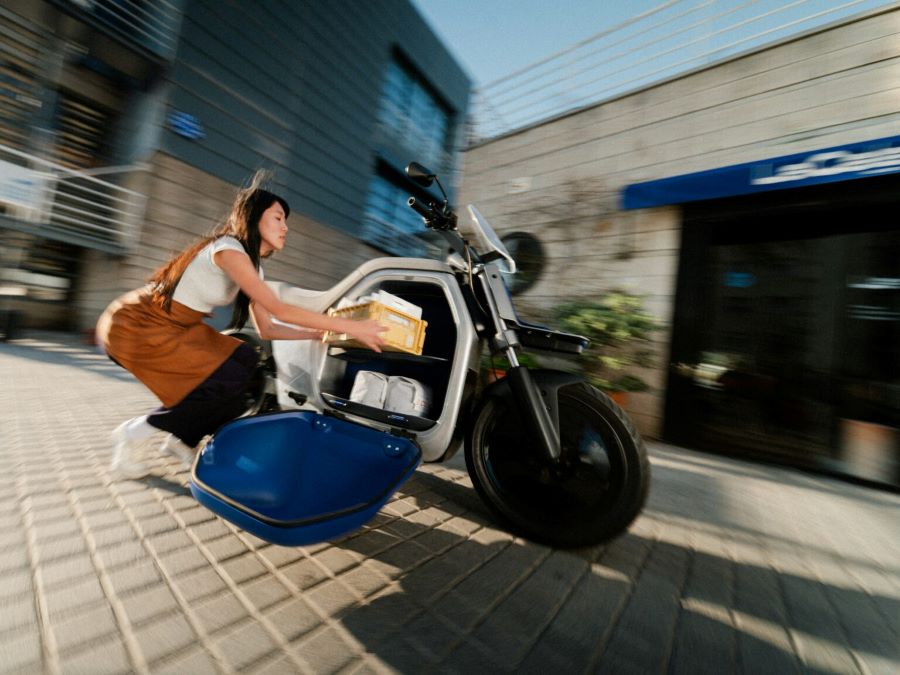 Una mujer con delantal introduce objetos en el interior del espacio de carga de una moto ANY LUV 1