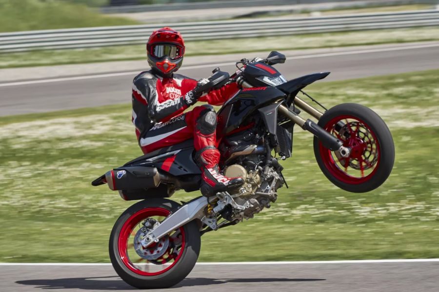 Una Supermotard Ducati total black con alma de superbike un piloto mira a la cámara mientras realiza un caballito con su Ducati Supermotard