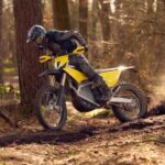 Un piloto, parado sobre las estriberas, maniobra una moto Radian EXR en un sendero boscoso.
