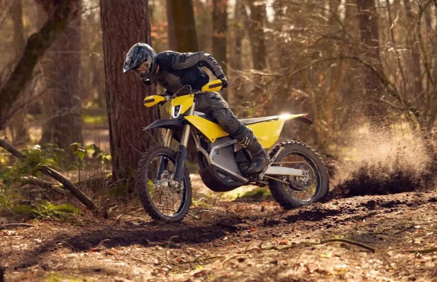 Un piloto, parado sobre las estriberas, maniobra una moto Radian EXR en un sendero boscoso.