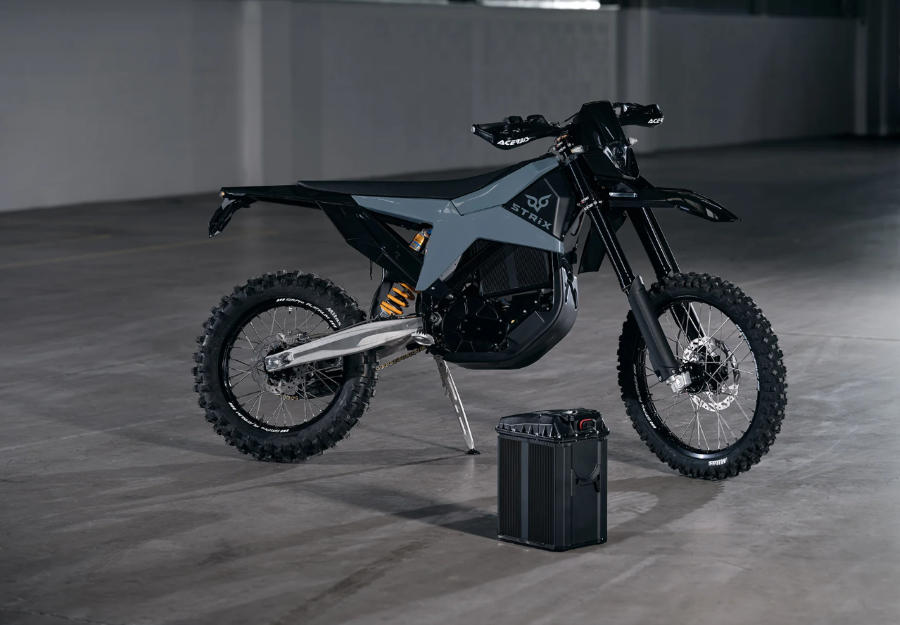 una moto eléctrica Strix Hard Enduro posa al lado de una batería