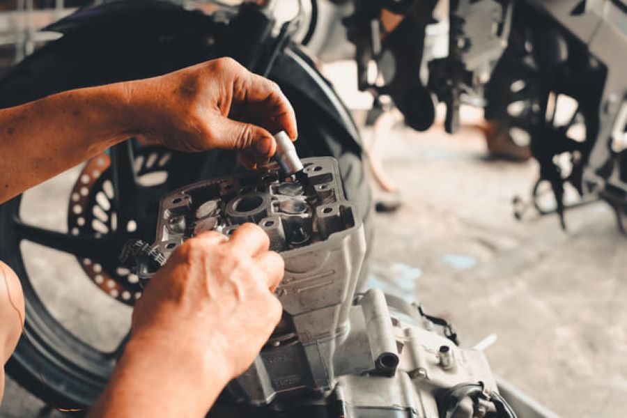 Las manos de un mecánico trabajan en una tapa de cilindros de moto