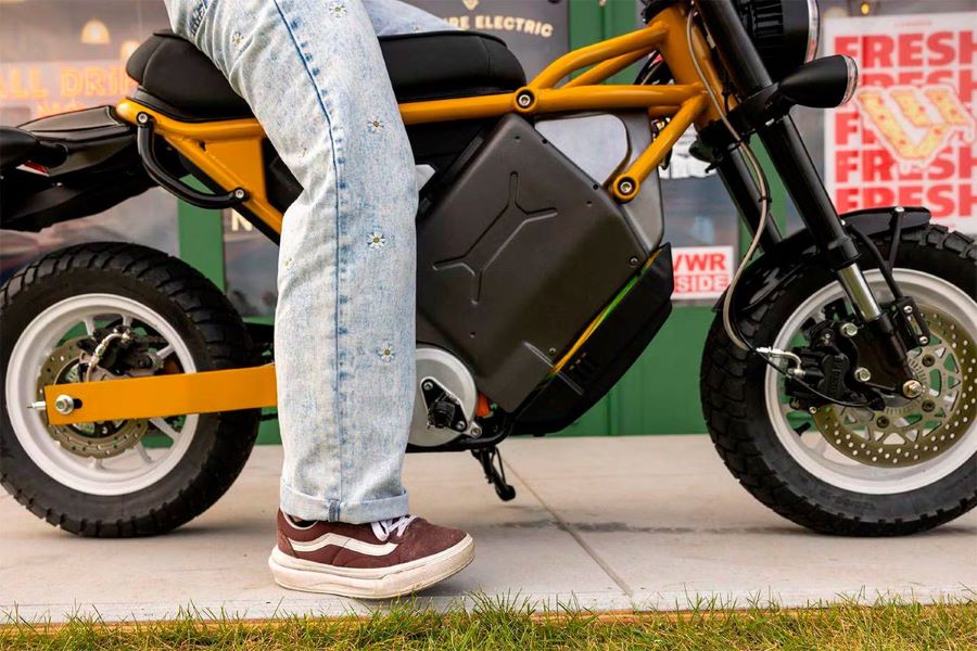 Una pierna vestida con jeans y zapatillas muestra a un joven sentado sobre una mini moto Livewire honcho