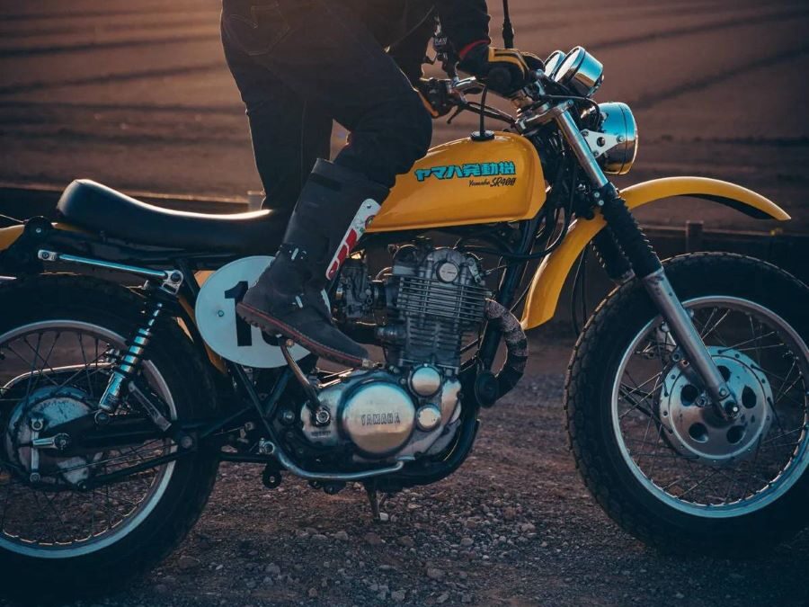 Un motociclista intenta arrancar su moto amarilla con una patada