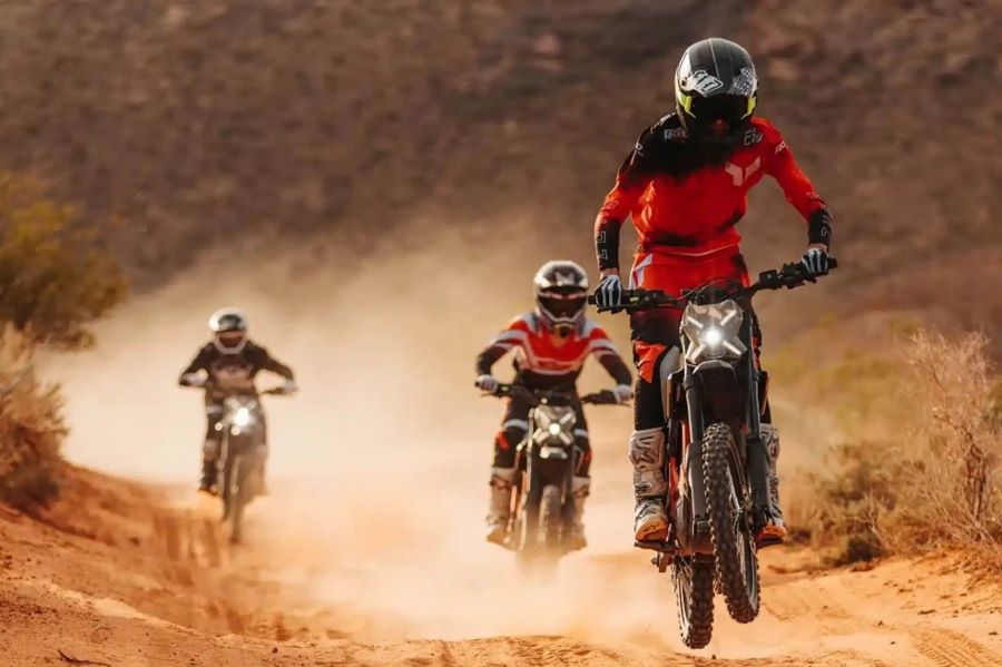 Tres pilotos vienen hacia la lente con sus motos eléctricas off-road con las luces encendidas