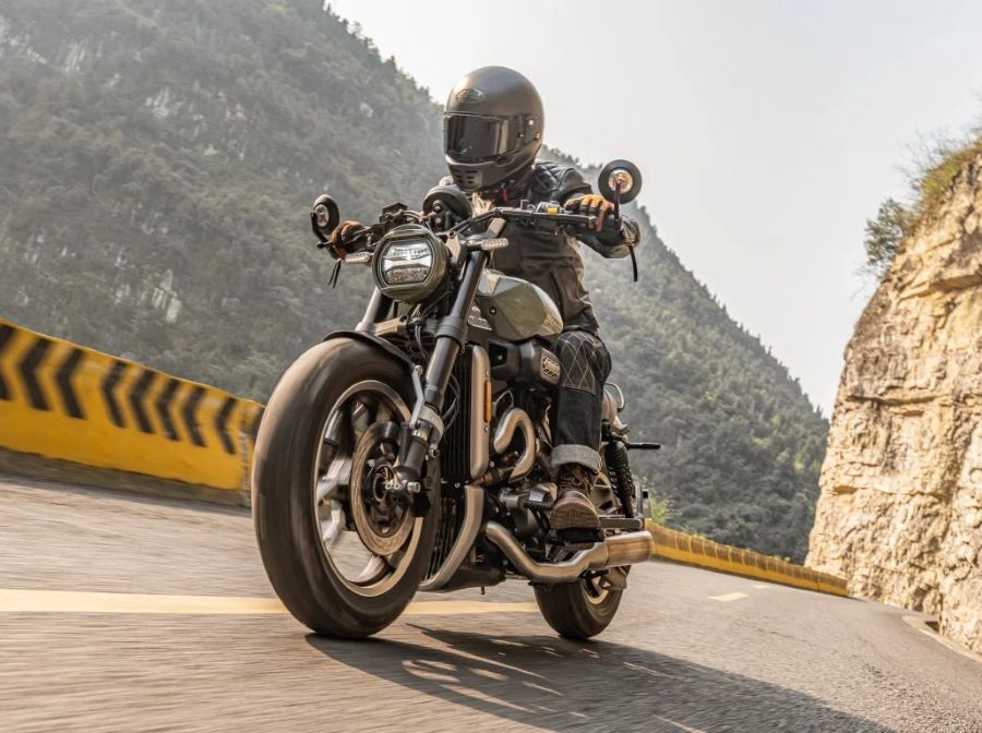 Vista en perspectiva delantera de una piloto que se traslada a bordo de una Hyosung GV250X Roadster en una ruta montañosa