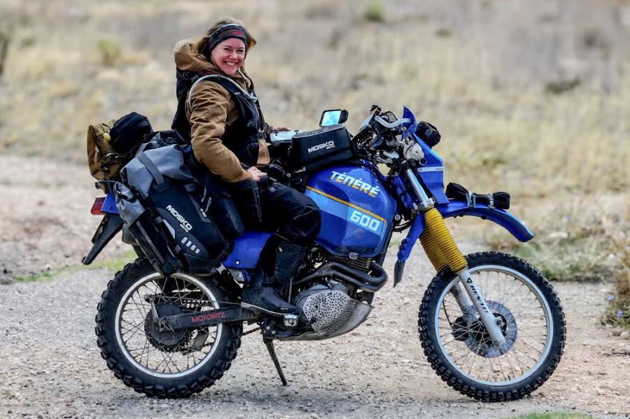 Itchy Boots sonríe encima de una moto off-road azul cargada de equipaje