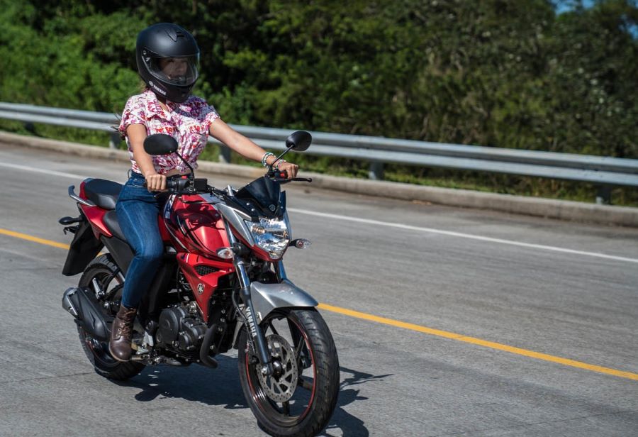 Una mujer se desplaza en una ruta con unan moto Yamaha 150 roja