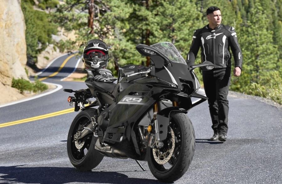 Un piloto se acerca a su Yamaha R9 2027 negra parada en el asfalto