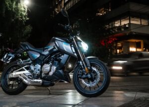 Una moto Malaguti Modena 300 gris posa delante de edificios iluminados en una ciudad