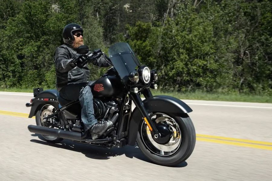 La Harley-Davidson Deadwood revive una historia olvidada Un motociclista avanza por una ruta flanqueada por un verde bosque a bordo de una moto Harley-Davidson Deadwood