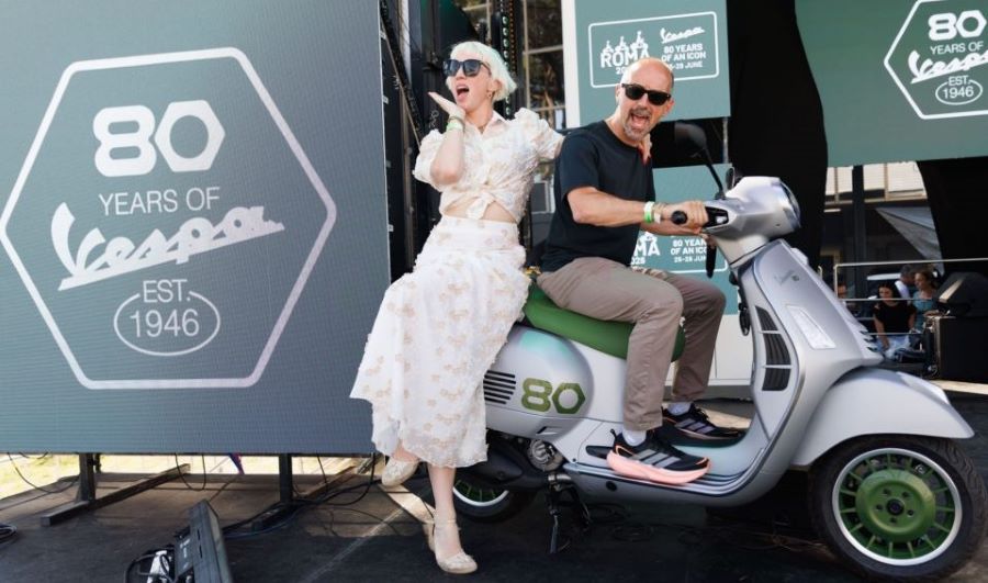Un hombre un una mujervestida con ropa de los 50 posan junto a una Vespa Edizione Ottantesimo