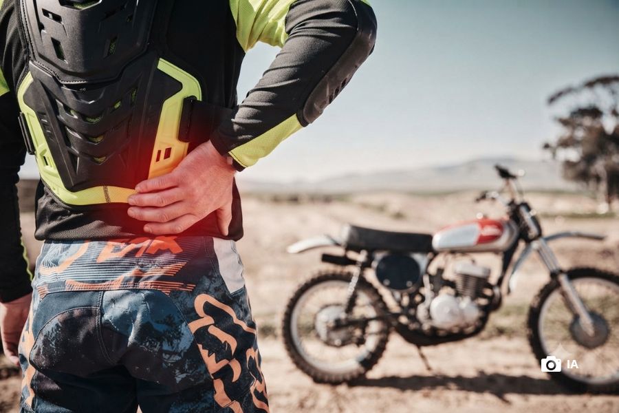 Dolores por andar en moto | Guía para identificar causas Un piloto de offroad se toma la parte baja de la espalda con dolor