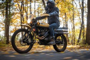 Un motociclista se traslada co una moto Janus por un bosque otoñal