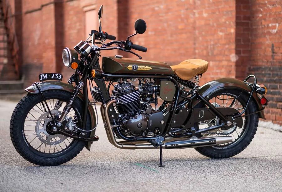 Una moto Janus Halcyon 450 Origin marrón posa delante de una pared rústica
