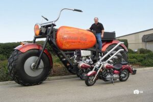 El creado de la moto más grande del mundo posa sobre la misma a la par de una Harley convencional