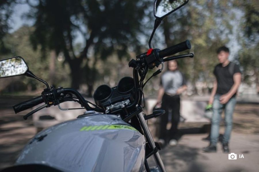 En primer plano, el tanque de una motomel S2, de fondo una pareja de jóvenes