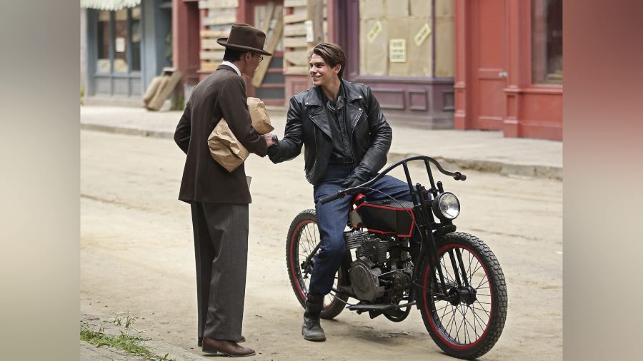 Una imagen de una escena de la serie Harley and the Davidsons en la que un joven sentado sobre una moto de la marca saluda a un hombre 