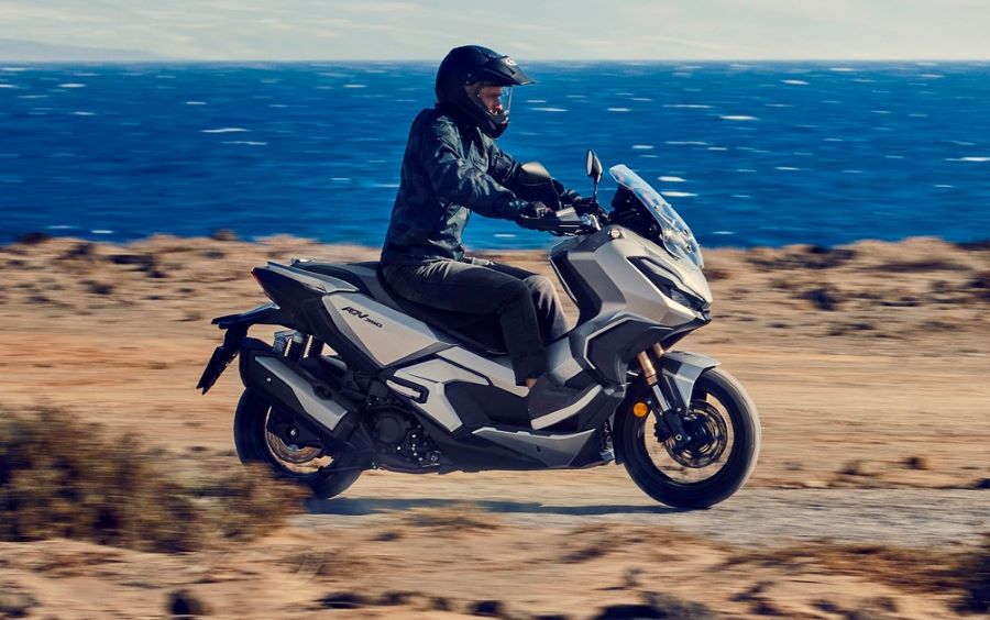 Cinco formas de entender el scooter crossover moderno Un Scooter Honda ADV 350 surca la tierra a un costado del mar azul