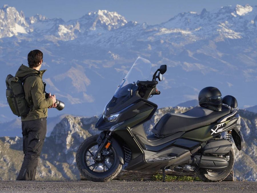 Cinco formas de entender el scooter crossover moderno Un usuario se apresta a tomar una foto cerca de un acantilado con su scooter crossover Kymco DTX 360 a su lado