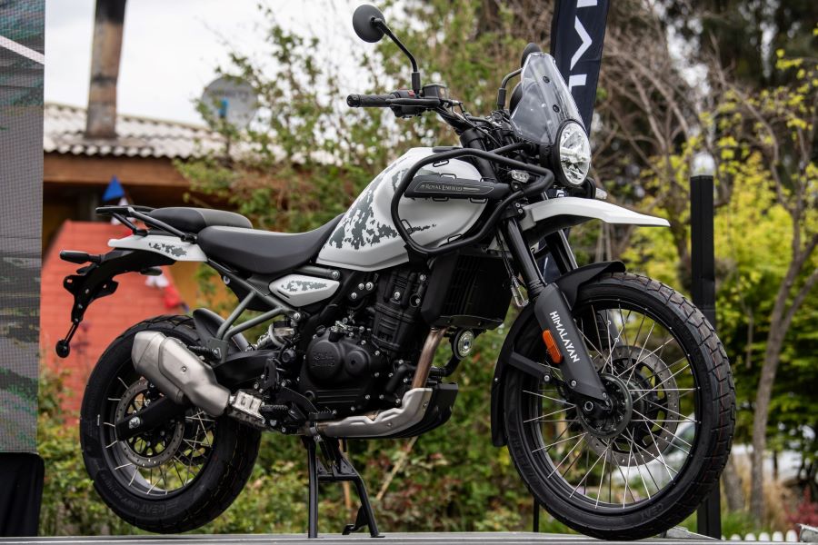 una Royal enfield Himalayan 450 blanca posa cerca de una vivienda campestre