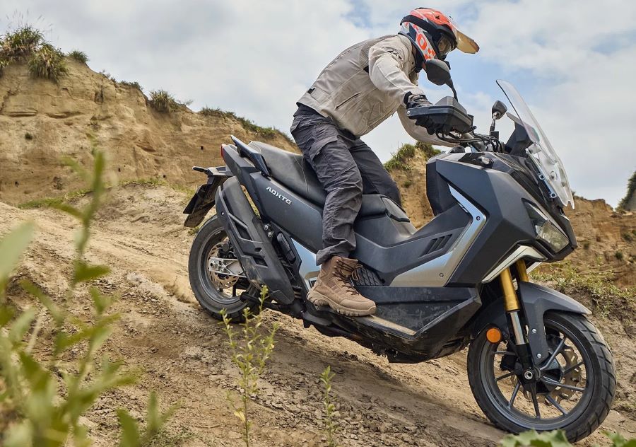 Cinco formas de entender el scooter crossover moderno Un usuario baja una empinada cuesta sobre su SYM ADXTG 400