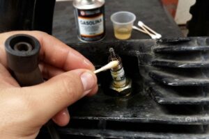 un mecánico limpia una bujía de moto con un hisopo empapado en gasolina.