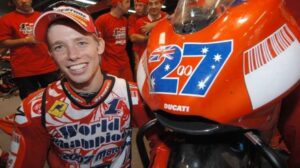 Medio cuerpo de Casey Stoner al lado de su Ducati con el característico número 27