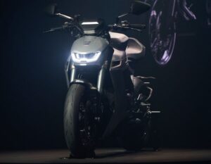 Una Norton Manx con las luces encendidas posa de frente en un stand