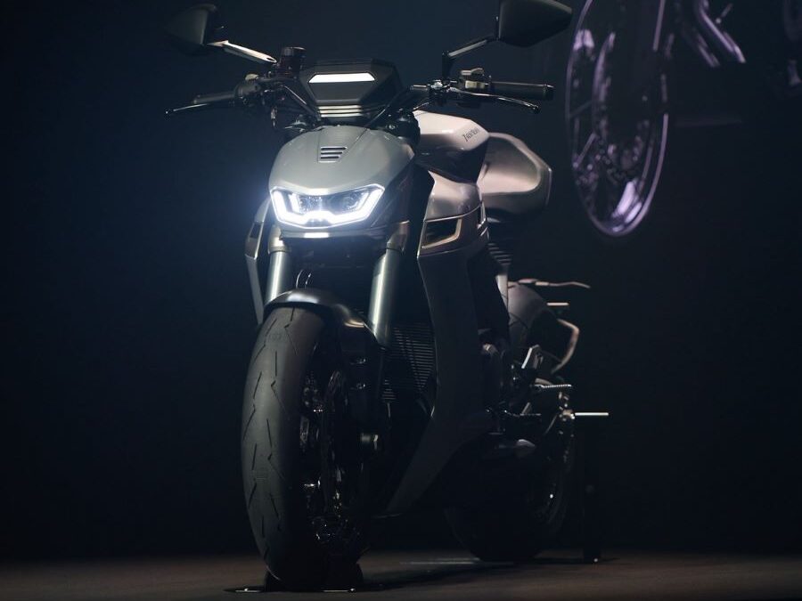 Una Norton Manx con las luces encendidas posa de frente en un stand