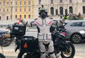 Un motociclista, vestido con ropa Lovo, posa delante de su moto Touring y de edificios antiguos