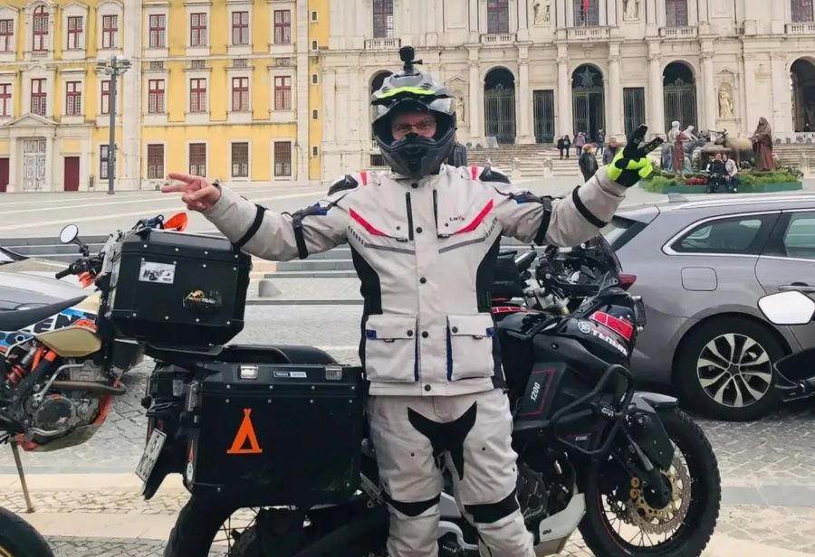 Un motociclista, vestido con ropa Lovo, posa delante de su moto Touring y de edificios antiguos