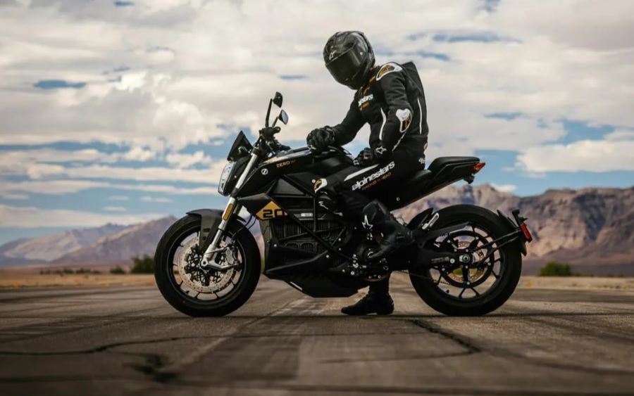 Un piloto, con mono y casco negros, posa sobre una moto Zero SR/F 20 Aniversario