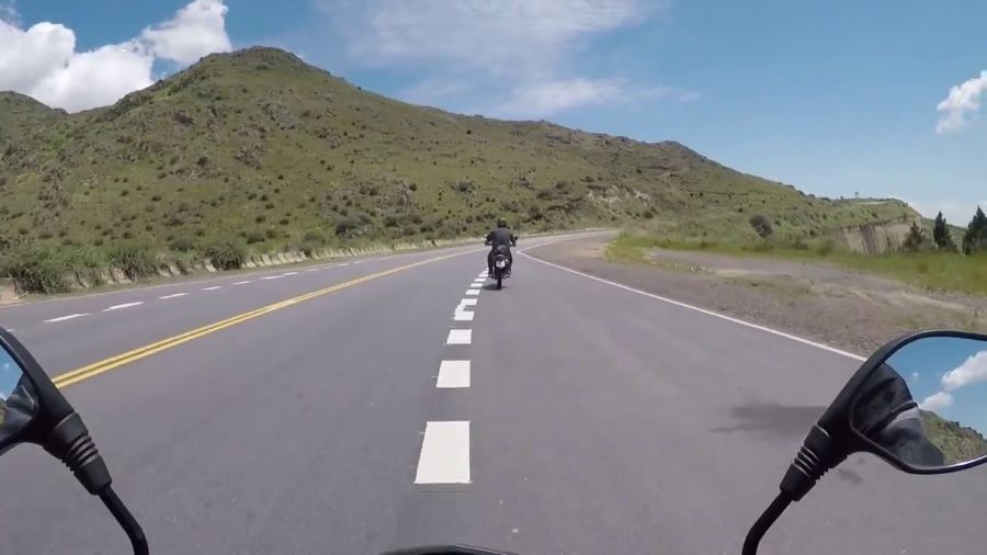 Un motociclista fotografía a otro que viaja adelante por el Camino de la Altas Cumbres
