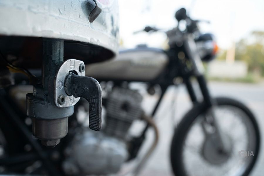 En primer plano una llave de paso de gasolina, detrás, una moto difusa
