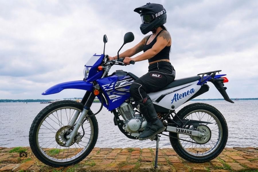 Una mujer monta una moto enduro azul con la leyenda Atenea en la cacha trasera