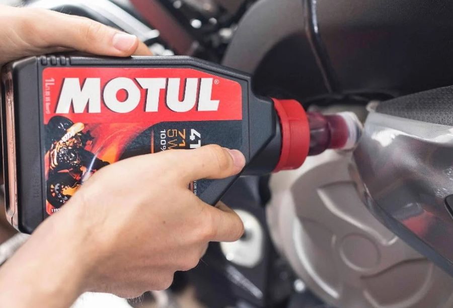 Dos manos vierten aceite Motul en un tanque de moto