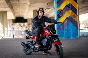 Un joven mira a la cámara sentado sobre su Corven Flow 150 roja ubicada debajo de un puente de autopista