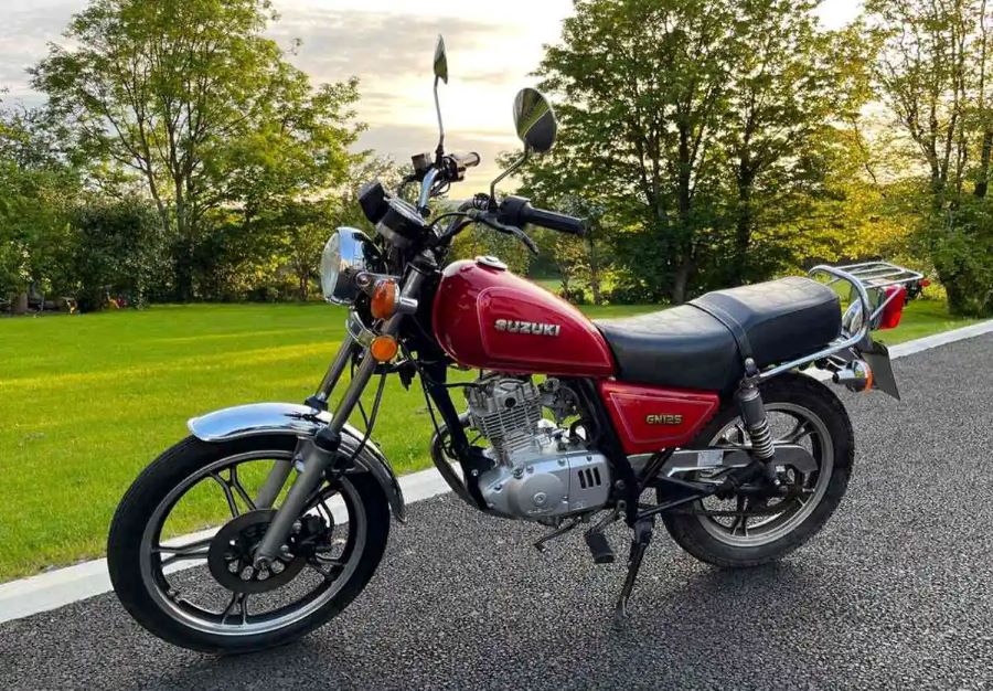 Lateral izquierdo de una moto Suzuki GN125 roja parada n un espacio verde