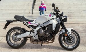 En primer plano, una Yamaha XSR900 2027, detrás un piloto sube por una escalera urbana
